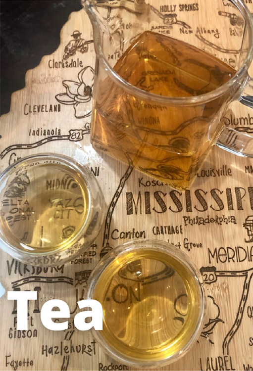 Picture of yellow hued tea in a pitcher and 2 glasses on wooden surface that is the map of the Mississippi